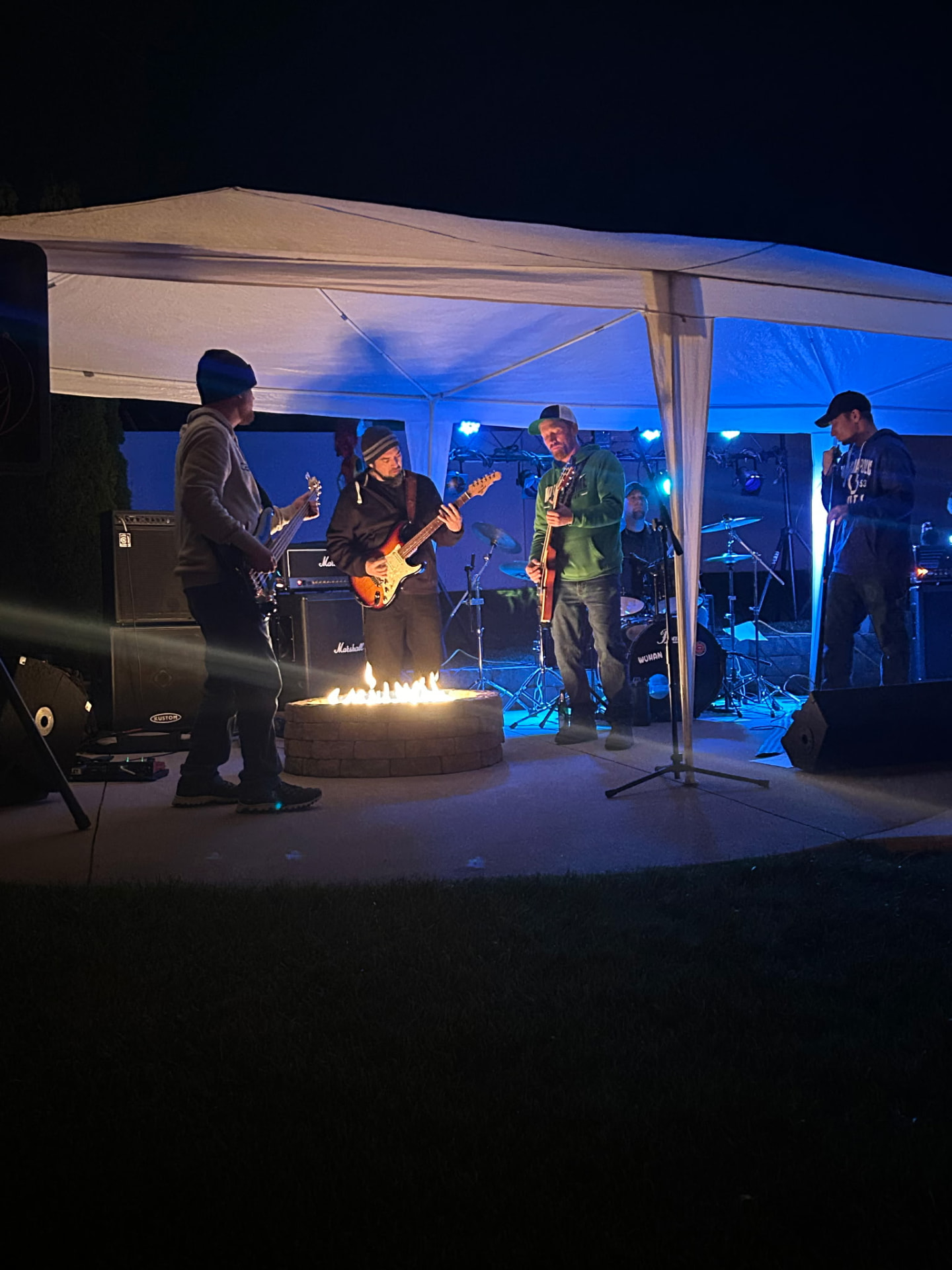 The band playing around a lit fire pit under blue stage light