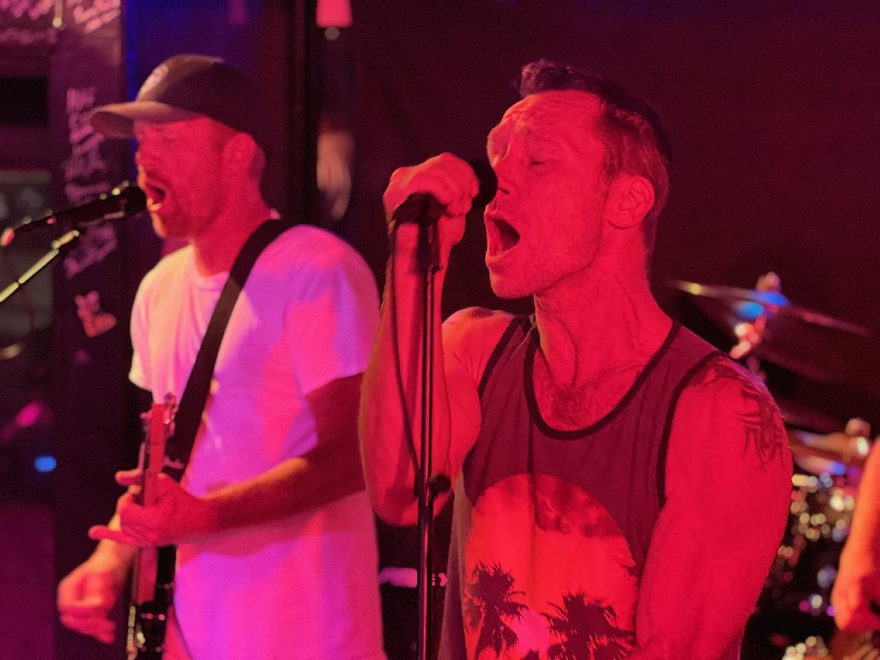 Singer and guitarist sharing vocals under red stage light